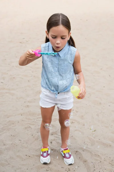 Pleine longueur vue de fille en short soufflant bulles de savon à l'extérieur — Photo de stock