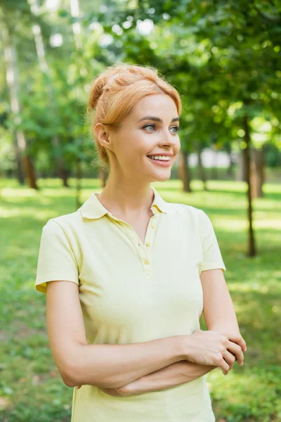 Pretty and happy woman standing with crossed arms in park — Stock Photo