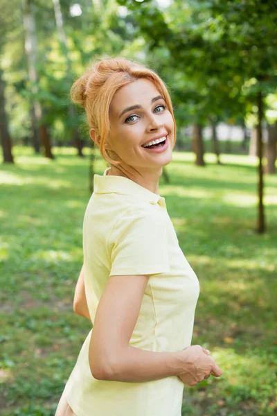 Mujer pelirroja emocionada mirando a la cámara en el parque de verano - foto de stock