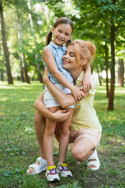 Full length view of happy mother and daughter in summer clothes embracing in park — Stock Photo