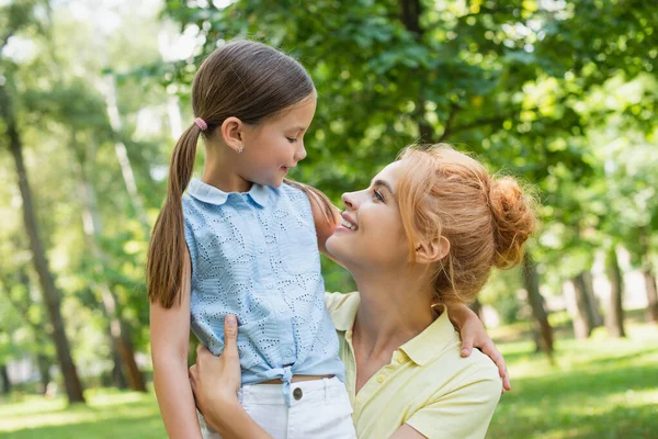 Mujer alegre y su hija abrazándose y mirándose en el parque de verano - foto de stock