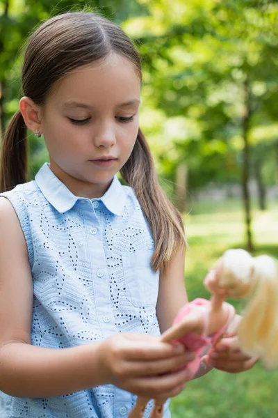 Girl in sleeveless blouse holding blurred doll outdoors — Stock Photo