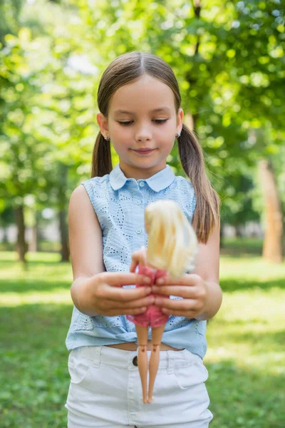 Задоволена дівчина в без рукавів блузка грає з лялькою в парку — стокове фото