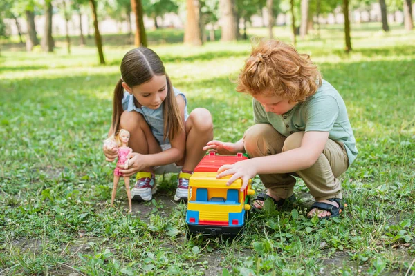 Irmão e irmã brincando com caminhão de brinquedo e boneca no gramado verde no parque — Fotografia de Stock