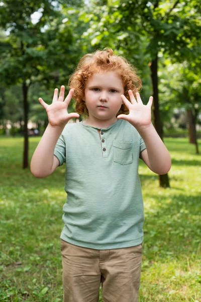 Menino em t-shirt mostrando palmas limpas enquanto olha para a câmera ao ar livre — Fotografia de Stock