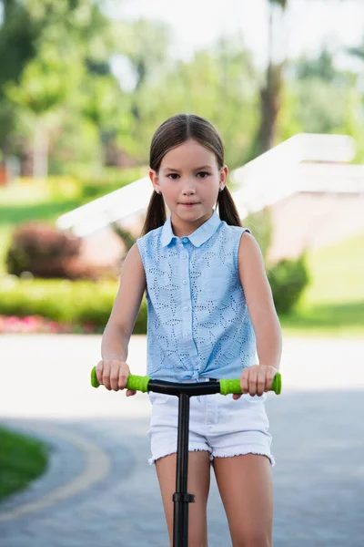 Chica con patada scooter sonriendo a la cámara mientras pasar tiempo en el parque - foto de stock