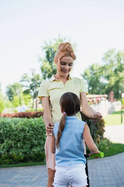 Femme souriante touchant les cheveux de sa fille tout en se tenant debout à l'extérieur — Photo de stock