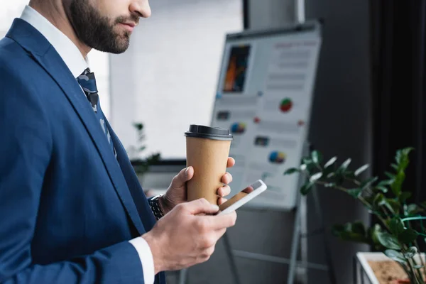 Teilansicht des Ökonomen mit Coffee to go mit Handy im verschwommenen Büro — Stockfoto