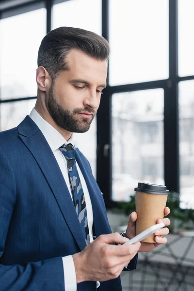 Economista bruna con bevanda da asporto utilizzando il telefono cellulare in ufficio — Foto stock