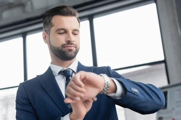 Low angle view of bearded businessman checking time on wristwatch — Stock Photo