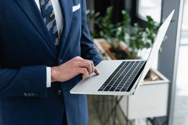 Cropped view of businessman using laptop while standing in office — Stock Photo