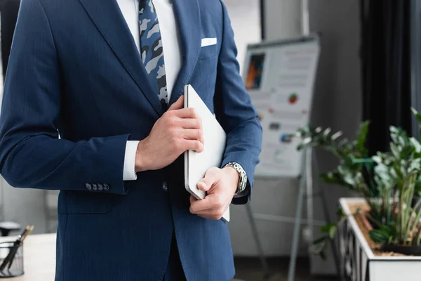 Partial view of economist standing with laptop in blurred office — Stock Photo