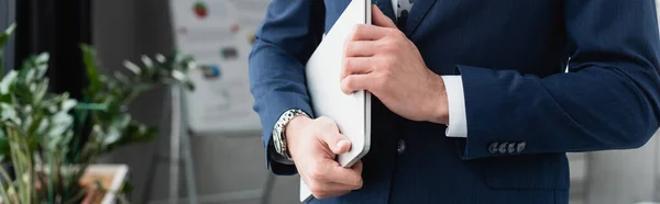 Vista ritagliata di uomo d'affari in giacca blu che tiene il computer portatile in ufficio, banner — Foto stock