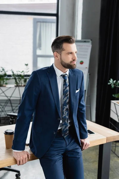 Economist in suit standing at workplace in office and looking away — стоковое фото