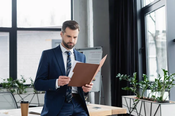 Economist looking in folder while standing near desk in office — стоковое фото