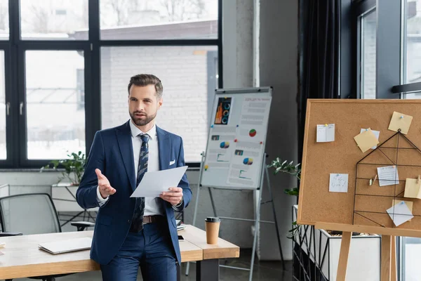 Economist pointing with hand while talking near corkboard with sticky notes — стоковое фото