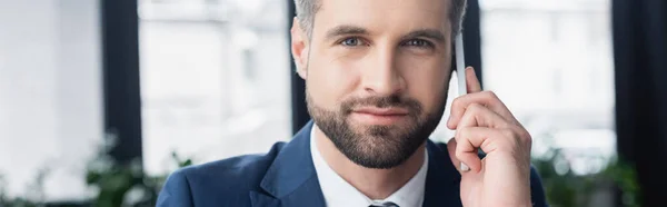 Bärtiger Geschäftsmann mit Smartphone im verschwommenen Büro, Banner — Stockfoto