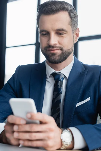 Messagerie économique positive sur téléphone portable flou dans le bureau — Photo de stock