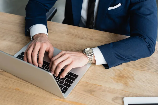 Cropped view of businessman in wristwatch typing on laptop in office — Stock Photo