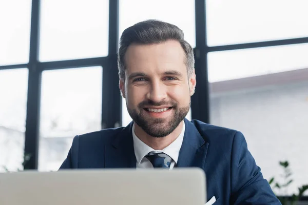 Retrato de hombre de negocios barbudo feliz mirando a la cámara en primer plano borroso - foto de stock