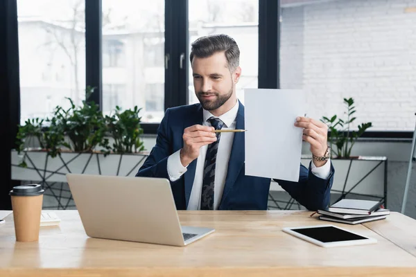 Economist pointing at empty paper during online conference on laptop in office — стоковое фото