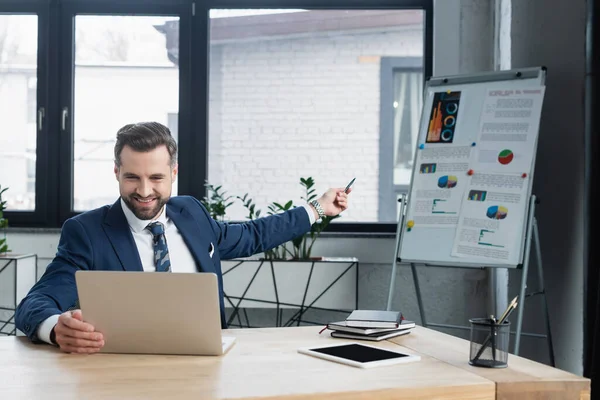 Happy economist pointing at flip chart with analytics during online conference on laptop — Stock Photo