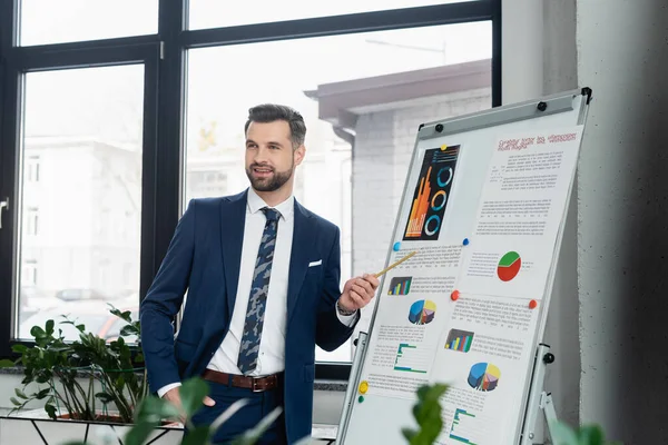 Economista positivo apuntando a la analítica en el rotafolio y mirando hacia otro lado en la oficina — Stock Photo