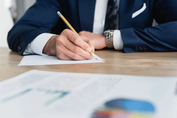 Partial view of economist writing with pencil in office on blurred foreground — Stock Photo