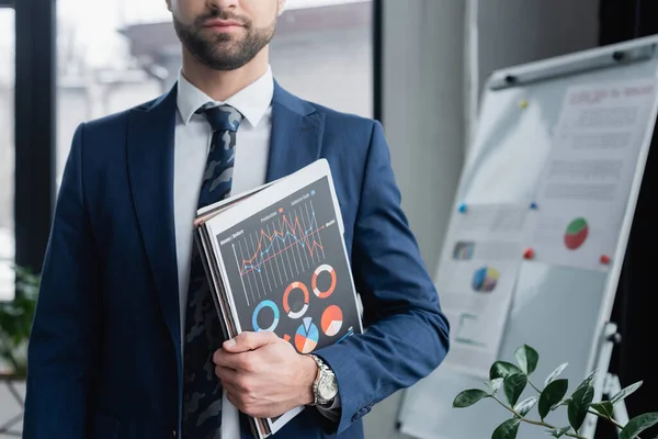 Cropped view of economist in blazer holding folders and infographics — Stock Photo