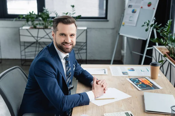 Glücklicher Ökonom, der am Arbeitsplatz im Büro in die Kamera blickt — Stockfoto