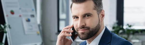 Uomo d'affari barbuto che parla al cellulare e guarda la telecamera in ufficio, banner — Foto stock