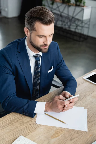 Brünetten Ökonomen mit Handy in der Nähe von Zeitungen und Bleistift auf dem Schreibtisch — Stockfoto