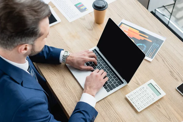 Vista aerea di economista digitando sul computer portatile con schermo vuoto vicino calcolatrice e caffè da andare — Foto stock