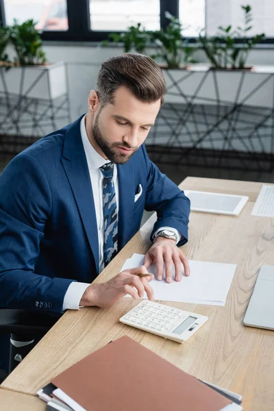 Comptable en costume à l'aide d'une calculatrice tout en travaillant au bureau — Photo de stock