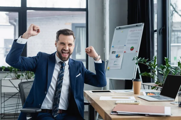 Économiste excité montrant geste de succès près du bureau au bureau — Photo de stock