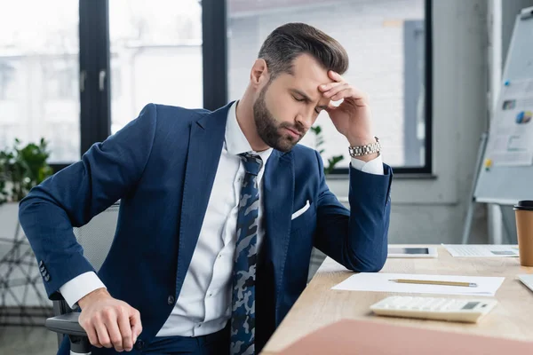Exhausted accountant sitting with closed eyes near blurred calculator on desk — Stock Photo