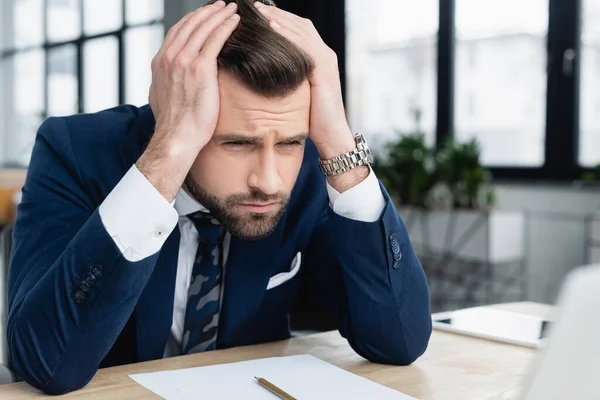 Homme d'affaires mécontent tenant la main sur la tête tout en étant assis sur le lieu de travail — Photo de stock