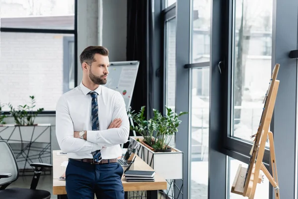 Economista in camicia bianca in piedi con braccia incrociate in ufficio e distogliendo lo sguardo — Foto stock