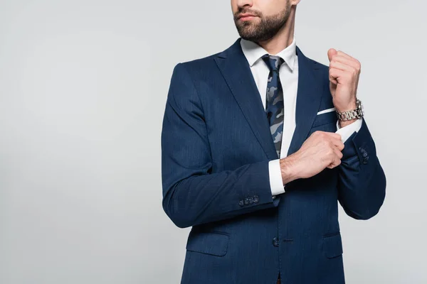 Cropped view of bearded businessman in blazer adjusting sleeve isolated on grey — стоковое фото