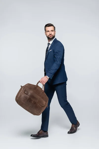 Vue pleine longueur de l'homme d'affaires marchant avec mallette en cuir et regardant loin sur gris — Photo de stock