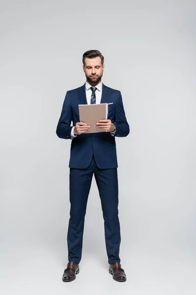 Full length view of businessman in blue suit holding folder on grey — Stock Photo