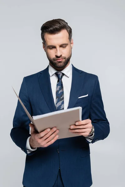 Brunette homme d'affaires en blazer bleu lisant des documents dans un dossier isolé sur gris — Photo de stock