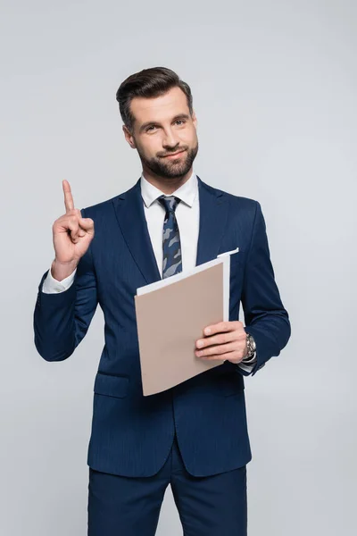 Позитивний бізнесмен тримає теку і показує жест ідеї ізольовано на сірому — стокове фото