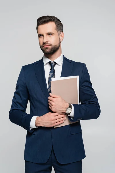 Hombre de negocios barbudo con carpeta mirando hacia otro lado aislado en gris - foto de stock