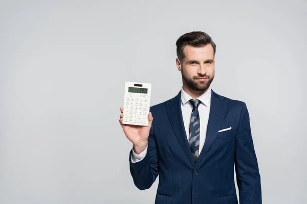 Morena economista mostrando calculadora y sonriendo a cámara aislada en gris — Stock Photo