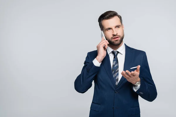 Economista en traje azul apuntando con la mano mientras habla en teléfono inteligente aislado en gris - foto de stock