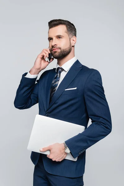 Hombre de negocios barbudo con portátil hablando en el teléfono móvil aislado en gris - foto de stock