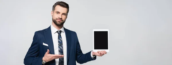 Uomo d'affari sorridente che punta al tablet digitale con schermo bianco isolato su grigio, banner — Foto stock