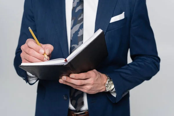 Cropped view of economist in blue blazer writing in notebook isolated on grey — Stock Photo