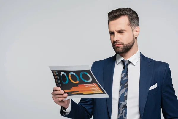 Pensive economist in blue blazer looking at paper with charts isolated on grey — стоковое фото